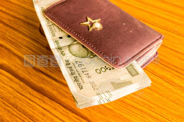 印度五百卢比现金纸币棕色钱包皮包在一张木桌上。